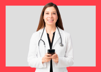 mulher de jaleco branco e aparelho de ouvir batimentos cardíacos segurando um celular nas mãos e sorri para a câmera