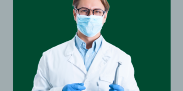 homem de máscara e jaleco branco segurando um aparelho de dentista