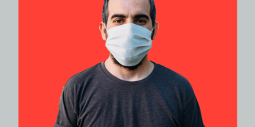 homem com máscara em frente a fundo vermelho e cinza