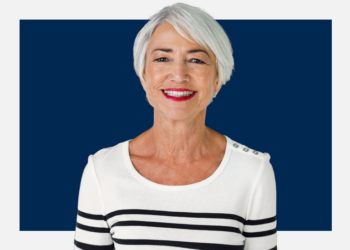 Mulher de cabelo grisalho e curto sorri para a câmera sob um fundo azul marinho e branco.