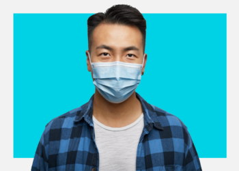 Homem oriental de máscara cirúrgica olha para a câmera sob um fundo branco e azul