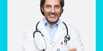 Médico de meia idade e braços cruzados olha para a câmera sobre um fundo branco e azul.