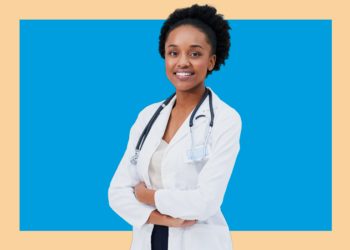 Médica olha para a câmera de frente de braços cruzados sobre fundo azul e bege.