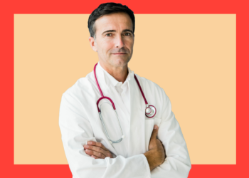 Médico branco olha para a câmera de braços cruzados sob um fundo bege e coral.