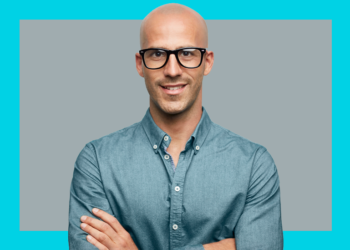 Homem olha e sorri para a câmera de braços cruzados sobre fundo cinza e azul