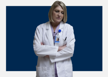 Médica olha pra baixo, cabisbaixa, sobre um fundo branco e azul marinho