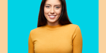 Mulher olha para a câmera sorrindo sobre fundo azul e bege