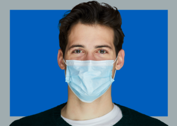 Homem de máscara cirúrgica olha pra câmera sobre fundo cinza e azul