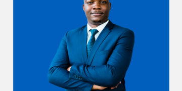 Homem de terno e braços cruzados olha para a câmera sobre um fundo azul e branco