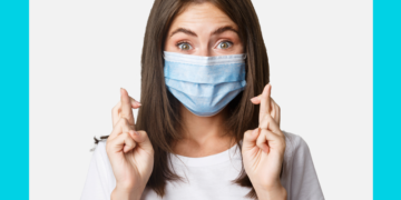 Mulher de máscara cirúrgica olha para a câmera e cruza os dados sobre um fundo azul e branco