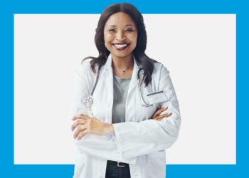 Médica de jaleco e estetoscópio sorri de frente para a câmera sobre um fundo branco e azul.