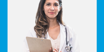Mulher de jaleco olha para a câmera com leve sorrido usando um jaleco. Fundo é branco e azul.