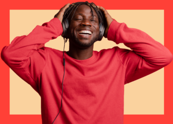 Homem de blusa vermelha e de fones de ouvidos sorri de olhos fechados sobre um fundo bege e coral.