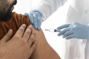 imagem ampliada de um médico aplicando vacina em paciente que usa camisa laranja